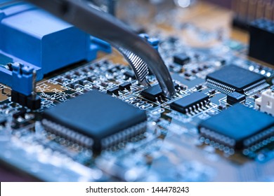 Close up on tweezers holding chip on computer circuit board. - Shutterstock ID 144478243