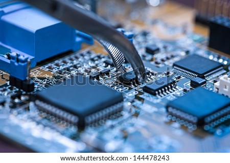 Close up on tweezers holding chip on computer circuit board.
