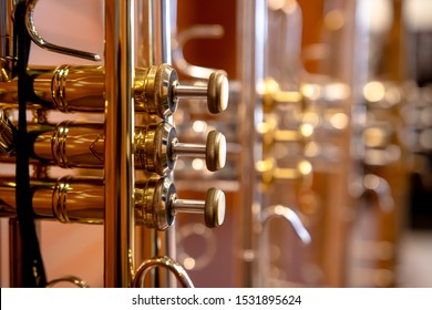 Close up on a valve section of a professional trumpet with other trumpets blurred out behind it.