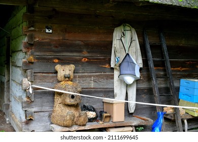 A close up on the wall of an old abandoned building with a beekeper suit handing from it and located next to some beekeeping equipment and a cute teddy bear made out of thatch and hay seen in Poland