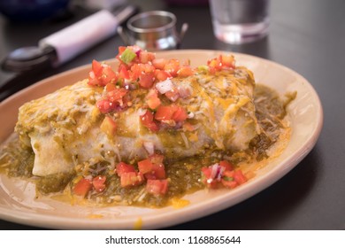 Close Up On A Wet Burrito Topped With Green Chili Sauce And Pico De Gallo Salsa, At A Mexican Restaurant 