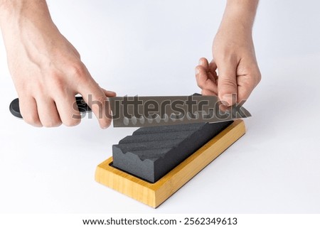 close up on a white background on a table, man hands sharpen a steel knife protection against cuts, a black medium-hard stone for sharpening knives professional knife for slicing vegetables