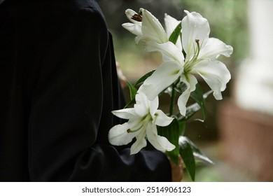 Close up on white lilies in hands of unrecognizable person wearing black suit while raindrops gently dripping on delicate petals, copy space - Powered by Shutterstock