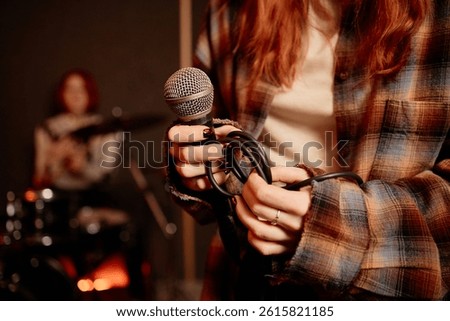 Close up on wire microphone in hands of female vocalist performing music with band in recording studio, copy space