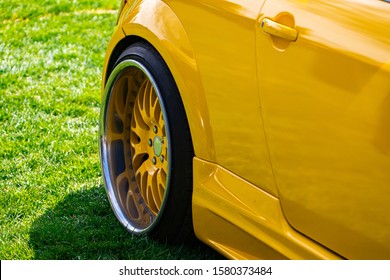 close up on yellow sports car rear wheel on grass, coupe small car with tuning is the modification, wheel with a large chrome rim and yellow interior