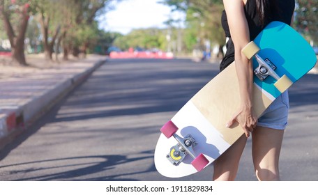 Close up on young women hand hold skateboard, surf skate on public park background. Free relax skateboard trendy concept. Fashion portrait of female hands holding surf skateboard