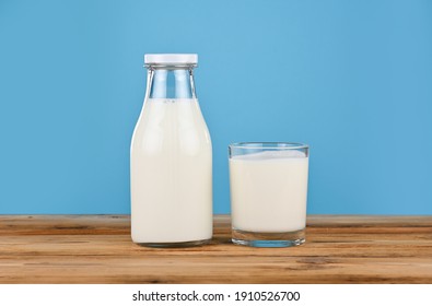 Close up one bottle and one drinking glass full of fresh milk on wooden table over blue background, low angle, side view - Powered by Shutterstock