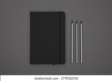 Close Up One Closed Black Leather Cover Notebook And Pencils Over Grey Paper Background, Flat Lay, Directly Above