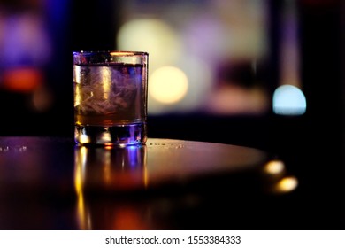 close up one glass of cocktail on wooden bar table in darkness.  Blurred lights background - Powered by Shutterstock