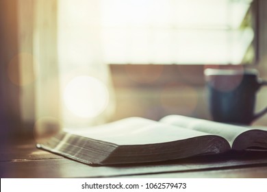 close up of open bible with acup of coffee for morning devotion on wooden table with window light