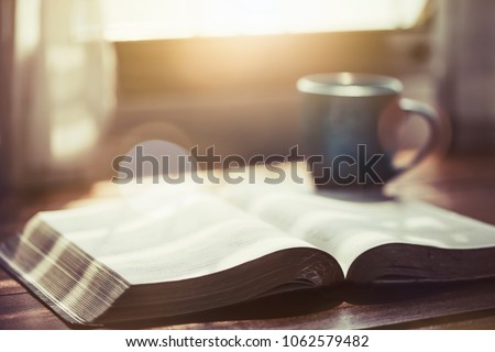 close up of open bible with a cup of coffee for morning devotion on wooden table with window light