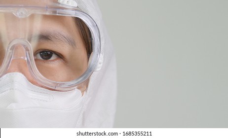 Close up open eye of Asian doctor in protective hazmat PPE suit wearing face mask and eyeglasses with copy space
