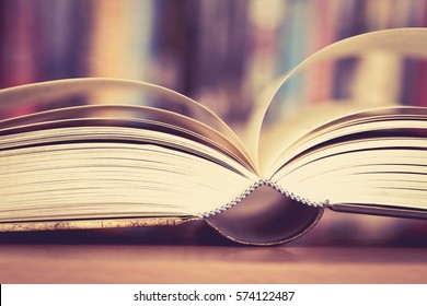 Close up opened book page with blurry bookshelf background for education and publication concept , extremely DOF with vintage retro color tone