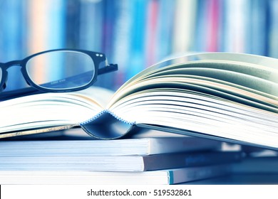 Close up opened book page and reading eyeglasses with blurry bookshelf background for education and publication concept - Shutterstock ID 519532861