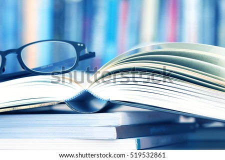 Close up opened book page and reading eyeglasses with blurry bookshelf background for education and publication concept