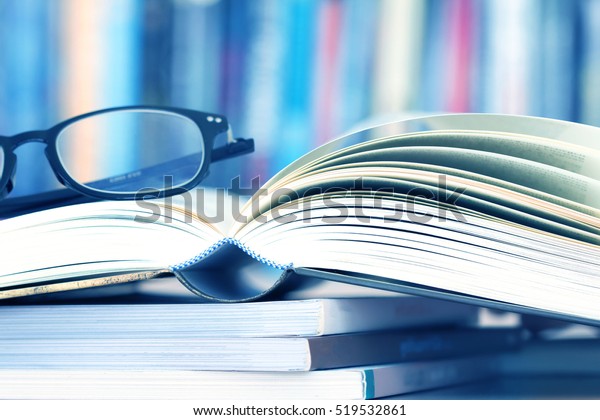 Close up\
opened book page and reading eyeglasses with blurry bookshelf\
background for education and publication\
concept