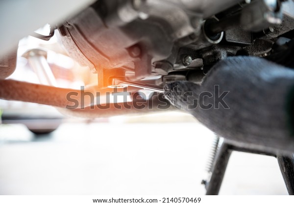 Close up open-end wrench in hand a man tighten\
wrench a nut on the oil pan: change the oil according to the\
distance of the\
motorcycle