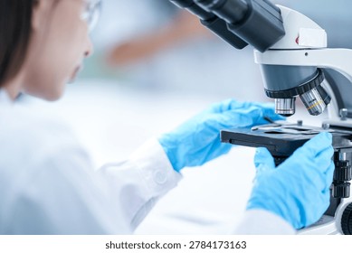 Close up optical microscope objective lens in science laboratory. Scientist hand in blue glove adjusting stage for high magnification biology analysis securely. Scientist checking biopsy slide sample.