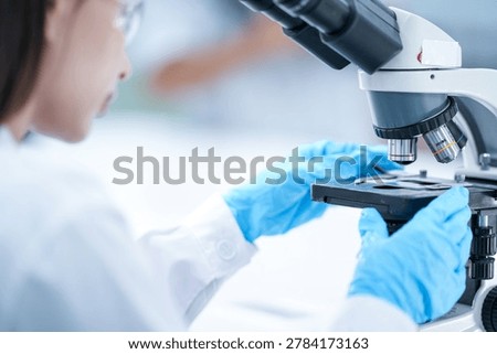 Close up optical microscope objective lens in science laboratory. Scientist hand in blue glove adjusting stage for high magnification biology analysis securely. Scientist checking biopsy slide sample.