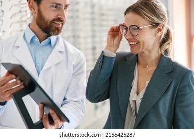 Close up of optometrist helping woman to choose glasses in optical store showing to her mirror - Shutterstock ID 2156425287