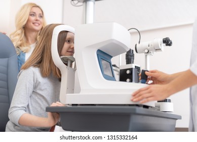 Close up of optometrist using auto refractometer while examining child eyes. Kid sitting in chair and smiling Stockfoto