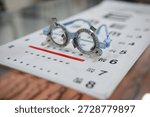 Close up of an optometry trial frame placed on an eye test chart with a colorful bokeh background. Concepts of vision testing, eye examination, ophthalmology, optician clinics, and eye care services.