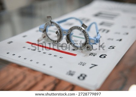Close up of an optometry trial frame placed on an eye test chart with a colorful bokeh background. Concepts of vision testing, eye examination, ophthalmology, optician clinics, and eye care services.