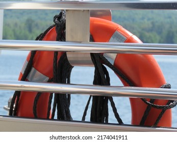 Close Up Of Orange Life Saver Floatation Device Hanging On Silver Metal Rails Of Boat Against Wild Forest And Lake Background
