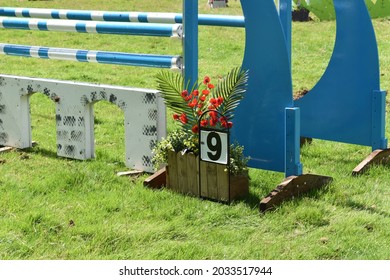 Close Up Of Outdoor Equine Show Jump Showing Its Spread, Brick Wall Filler, The Blue Wings, The Stripped Poles, The Number In The Jump Course And Floral Decoration For The Horse And Rider To Jump. 