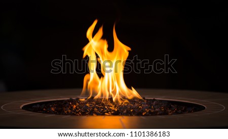 Close up of an outdoor fireplace with a big yellow flame and black background