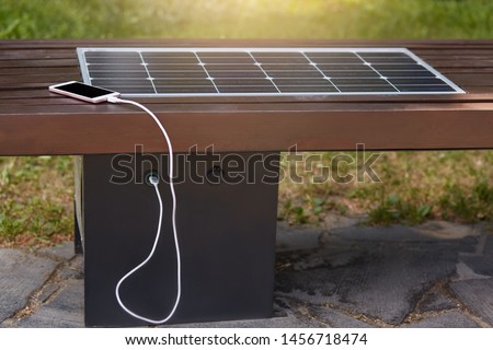 Close up outdoor image of smartphone charging via USB in park with help of solar panel installed inside wooden bench. Modern technologies, alternative sources of energy. Environment concept.