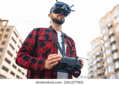 Close up outdoor portrait of a male professional fpv drone pilot wearing goggles and using remote controller to operate multicopter at the street. Focus is on hands.