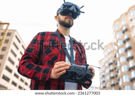 Close up outdoor portrait of a male professional fpv drone pilot wearing goggles and using remote controller to operate multicopter at the street. Focus is on hands.