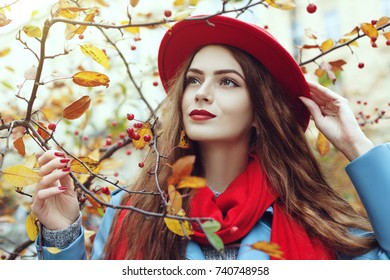 Close up outdoor portrait of young beautiful happy smiling girl wearing red hat and scarf posing near autumn tree. Model with red lips, long hair. Lady looking up.
 - Powered by Shutterstock