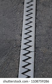 Close up outdoor view from above of an iron dilatation joint placed on a bridge road. Zigzag line drawn of an bright steel surface. Abstract design with grey geometric shapes on the asphalt ground.  