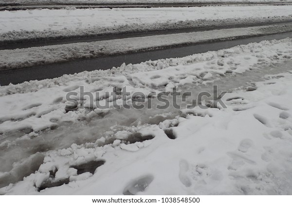 Close up outdoor view of car tracks and
footprints in the snow. Graphic design with grey convergente lines
and traces on the white surface. Abstract view of a snowy asphalt
road during the winter.