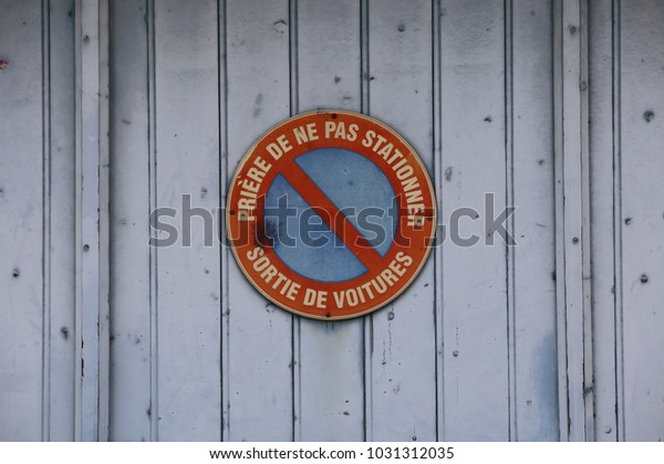 Close up outdoor view of a french circular sign fixed at\
an ancient blue garage door. On the symbol is written in french: no\
parking, car exit. Pattern with vertical lines and a circular form.\
 