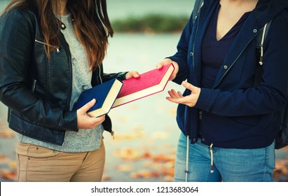 Close Up Outdoors Portrait Of Two Women Students Exchanging Books. Knowledge Sharing Between People. Give To Read To A Friend.