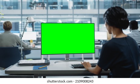 Close Up Over the Shoulder Shot of a Businesswoman Working on Desktop Computer with Chroma Key Green Screen Mock Up Display. Digital Projects Manager Typing Data, Using Keyboard and Mouse. - Powered by Shutterstock