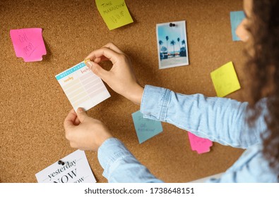 Close up over shoulder view of young african american woman pin weekly planning sticker on mood board at home office. Girl put many sticky note memo on noticeboard to organize life and work concept - Powered by Shutterstock