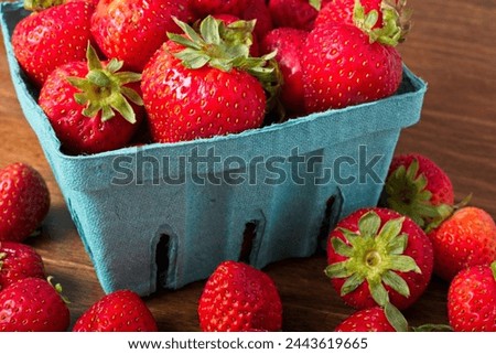 Close up overflowing quart pulp fiber basket of strawberries on a rustic wooden table. Part of the summer fresh fruit crop from the farmer's market