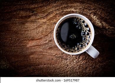 Close Up Overhead View Of A Cup Of Strong Frothy Espresso Coffee On A Rough Textured Wooden Surface With Dark Vignetting And A Highlight Around The Mug, With Copyspace