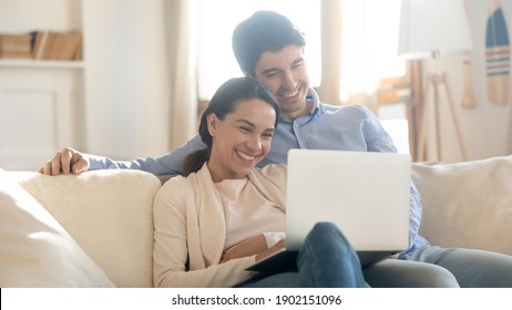 Close Up Overjoyed Couple Looking At Laptop Screen, Sitting On Cozy Couch At Home, Smiling Woman And Man Hugging, Using Computer, Booking Or Shopping Online, Enjoying Leisure Time With Device