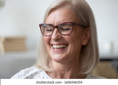 Close up of overjoyed mature female pensioner or grandmother in glasses laugh at funny joke, happy elderly woman smile showing white healthy teeth, orthodontic dental treatment, crown implementation