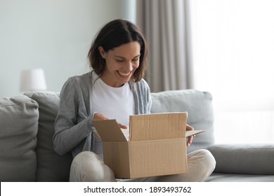 Close up overjoyed smiling young woman opening cardboard box with awaited parcel, sitting on couch at home, satisfied client received online store order, good quick delivery service concept
