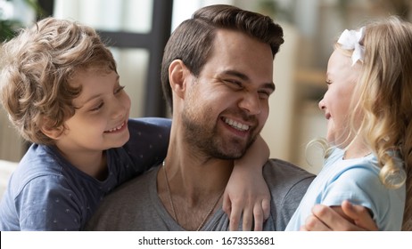 Close up of overjoyed young father laugh have fun with cute little kids relaxing together at home, excited loving dad playing with small preschooler children enjoying leisure time on weekend