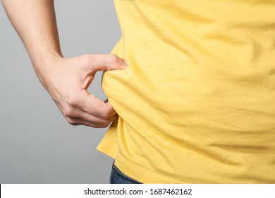 Close up of overweight obese man's hand holding his big belly isolated over gray background