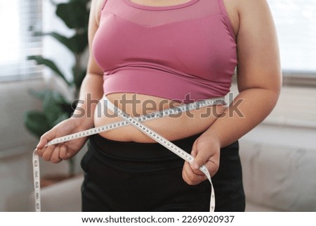 Close up overweight woman measuring her hip with tape measure.