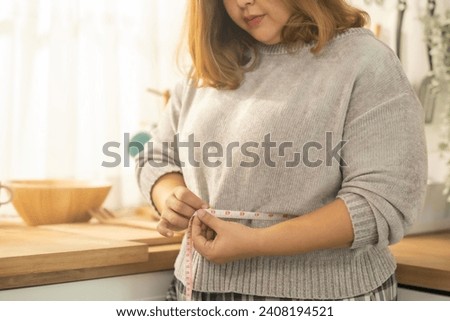 Close up Overweight woman measuring waist with tape on in kitchen with smile of progress for weight lose.