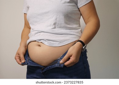 Close up of overweight young woman with fat belly after childbirth, pants doesn't fit, white background 